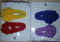 Four crocheted hair accessories in yellow, blue, red, and purple on a branded card.