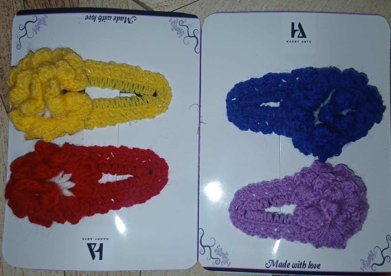 Four crocheted hair accessories in yellow, blue, red, and purple on a branded card.